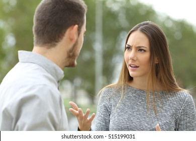 Couple talking seriously outdoors in a park with a green background