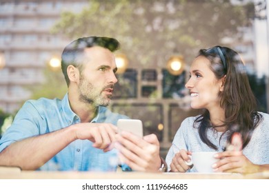 Couple talking and using smartphone while having coffee in cafe