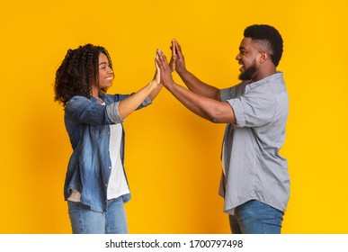 Couple Teamwork Concept. Joyful Black Couple Giving High Five To Each Other, Celebrating Common Success, Standing Over Yellow Background