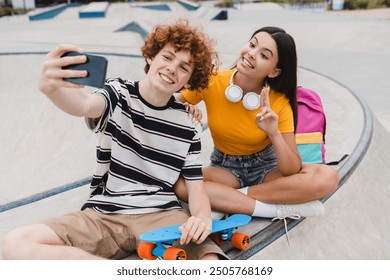 Couple of teenagers classmates students high school pupils friends boy girl bloggers in casual with skateboards bags taking selfie shot holding smart mobile phone having fun sitting on skate park ramp - Powered by Shutterstock