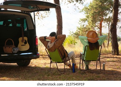 Couple with thermoses resting in camping chairs on autumn day, back view