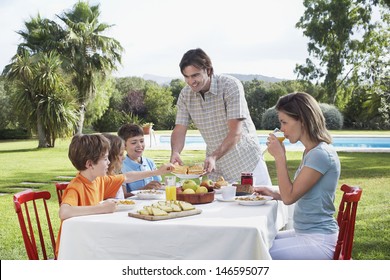 Couple with three children sitting at breakfast table outdoors - Powered by Shutterstock