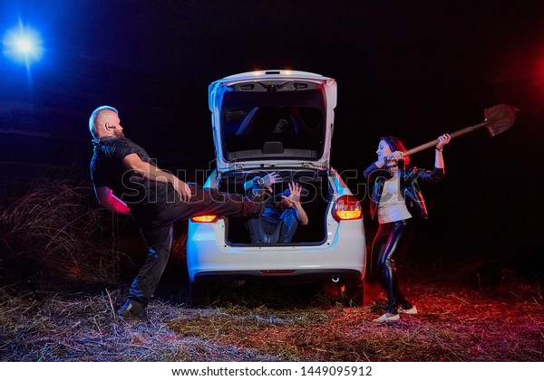 Couple of thugs near car trying to\
kill young guy in the trunk at night time and colored red and blue\
light around. Photoshoot about life of gungsters in\
Russia