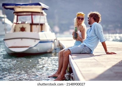 Couple Toasting With Beer Sitting By Water On Wooden Jetty. Holiday, Lifestyle, Togetherness Concept.