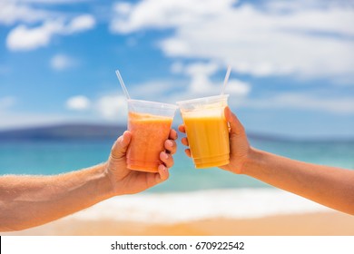 Couple toasting healthy juice drinks together at beach restaurant. Detox smoothie drink toast at summer vacations holidays. Fruit juicing weight loss diet.