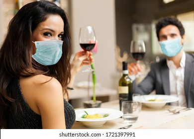 Couple toasting wineglasses in a luxury restaurant and wearing masks, coronavirus concept