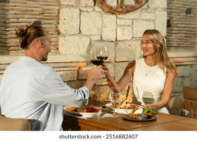 A couple toasts with their wine glasses, celebrating a wonderful evening meal at a cozy outdoor restaurant - Powered by Shutterstock