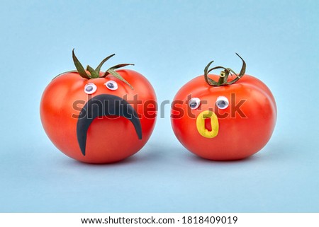 Couple of tomatoes with funny faces. Concept of healthy eating and living. Isolated on blue background.