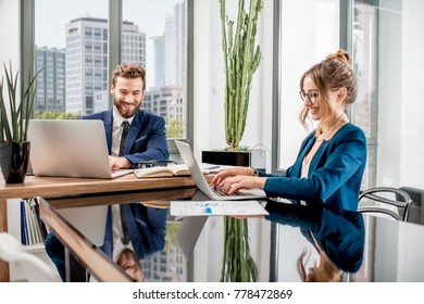 Couple of top managers working with laptops and documents sitting at the luxury office interior with beautiful view on the skyscrapers