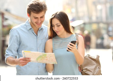 Un par de turistas consultando a un guía de la ciudad y gps de teléfonos móviles en una calle
