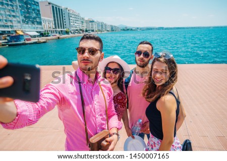 Couple of tourists is exploring new city together. Smiling and takeing a selfie, next to the sea.