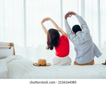 Couple Of Tourists, Happy Holiday. Summer Vacation. Portrait Of Back View Of Young Asian Man And Woman Stretching With Relaxing With Beach Hat On White Bed Near Curtain At The Window In Hotel Room.