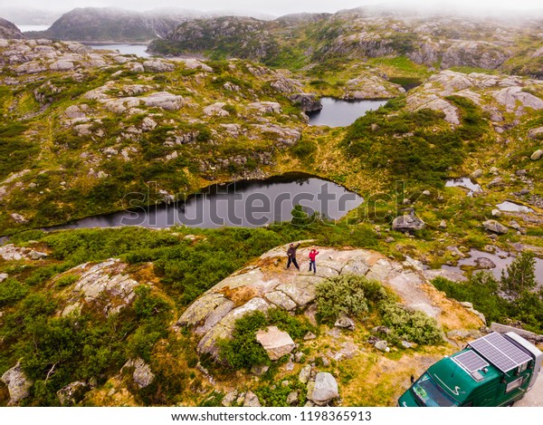 Couple tourists peolpe and\
motorhome camper car with solar panels on roof in rocky mountains\
landscape, Norway. Norwegian national tourist scenic route\
Ryfylke.