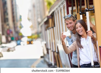 Couple tourists riding the popular touristic attraction cable car system in San Francisco city, California during summer travel holidays. People having fun taking selfie picture and tourist photos.