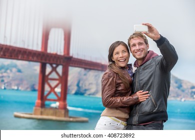 Couple tourists taking selfie photo in San Francisco by Golden Gate Bridge. Interracial young modern couple using smart phone by famous american landmark. Asian woman, Caucasian man. - Powered by Shutterstock