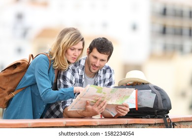 Couple of tourists talking checking paper map on vacation standing outdoors in a balcony in a rural town