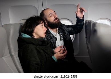 Couple of tourists waiting for flight to takeoff on airplane, being seated in economy class. Man asking flight attendant to help, flying with international airways plane to travel on holiday