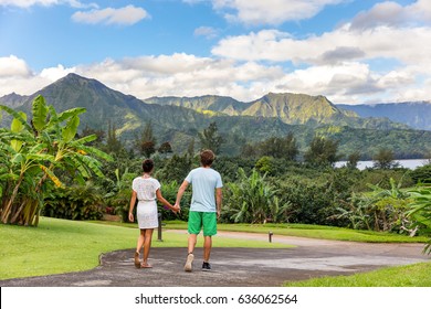 Couple tourists walking on Hawaii vacation. Two young people relaxing in Hanalei Bay resort in Kauai, Hawaii travel beach destination with Kauai mountains in the background.