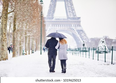 Couple of tourists walking in Paris under umbrella on a day with heavy snow. Unusual weather conditions in Paris - Powered by Shutterstock