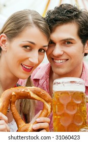 Couple in traditional German costume in a beer tent, he is having a drink, she a pretzel