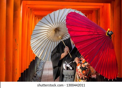 Couple With Traditional Japanese Umbrellas Posing At Torii Gates In Kyoto