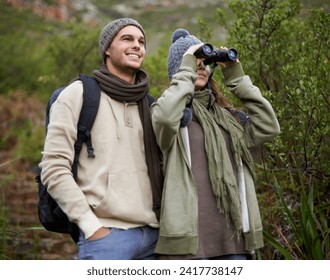 Couple, travel and binoculars in nature for hiking, adventure and journey or explore together in winter. Happy man and woman trekking with outdoor search, vision or birdwatching in forest or woods