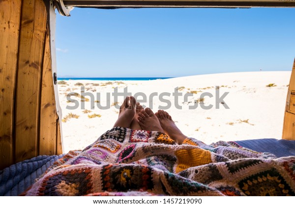 Couple of traveler feet love and live together the
travel wanderlust lifestyle in alternative summer vacation with old
wooden vintage van - coloured blancket and sea and beach view from
camper bed