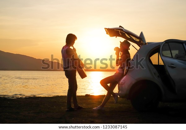 couple traveler\
have camera and guitar sitting on hatchback of car and looking for\
view of lake mountain and sunset near the dam on\
vacation.silhouette romance concept.\

