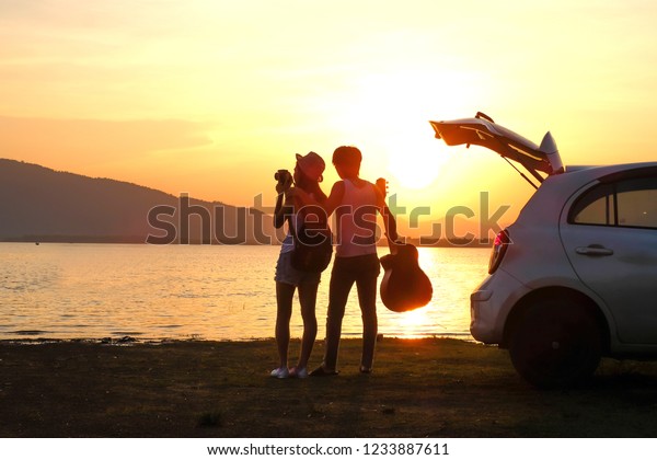 couple traveler
have camera and guitar sitting on hatchback of car and looking for
view of lake mountain and sunset near the dam on
vacation.silhouette romance concept.
