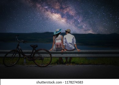 Couple Traveler Sitting Near A Bicycle And Looking For The Milky Way And Stars On The Sky At Night.silhouette Style.this Picture May Have Some Noise.