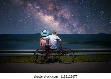 Couple Traveler Sitting Near A Bicycle And Looking For The Milky Way And Stars On The Sky At Night.silhouette Style.this Picture May Have Some Noise.