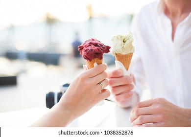 Couple of travelers are enjoying and holding ice cream in cones in their hands. Bride has wedding ring. Lovers have dating in sea resort during romantic honeymoon vacation at sunset outdoors. - Powered by Shutterstock