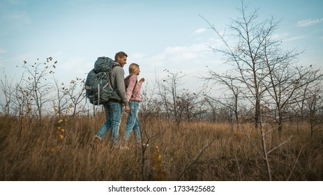 Couple Of Travelers Walking Through An Autumn Field Holding Hands. Tourists At Full Height Against A Background Of Blue Sky And Autumn Natural Landscape. Shot From Below. Hiking Concept.