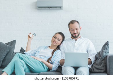 couple turning on air conditioner during the summer heat while using laptop