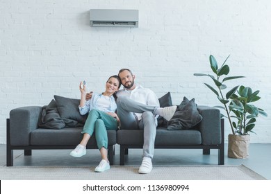 Couple Turning On Air Conditioner During The Summer Heat At Home  