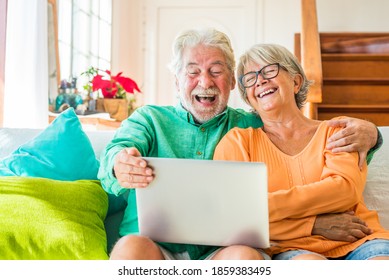 couple of two happy mature and old people or seniors at home sitting on the sofa enjoying and having fun laughing together looking and using a laptop or computer pc