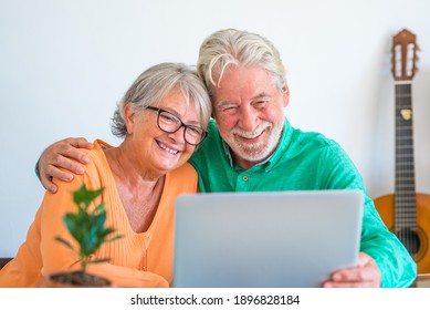 Couple Of Two Happy Mature And Old People Or Seniors At Home Sitting On The Sofa Enjoying And Having Fun Together Looking And Using A Laptop Or Computer Pc