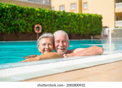 Couple of two happy seniors having fun and enjoying together in the swimming pool smiling and looking at the camera. Happy people enjoying summer outdoor in the water