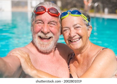 Couple of two happy seniors having fun and enjoying together in the swimming pool taking a selfie picture smiling and looking at the camera. Happy people enjoying summer outdoor in the water