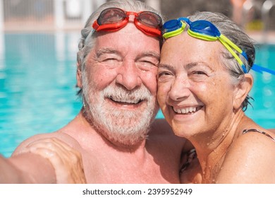 Couple of two happy seniors having fun and enjoying together in the swimming pool taking a selfie picture smiling and looking at the camera. Happy people enjoying summer outdoor in the water - Powered by Shutterstock