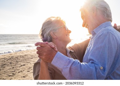 Couple of two old and mature happy seniors enjoying summer dancing together at the beach on the sand with the sunset at the background. Retired and leisure lifestyle - Powered by Shutterstock