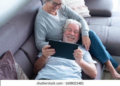 couple of two seniors or mature people at home having fun together looking at the same tablet - pensioner lying on the sofa with his wife sitting - Powered by Shutterstock