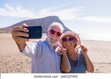 couple of two seniors takign a selfie together at the beach having fun in their vacations - happy mature old people smiling and looking at the camera of the phone