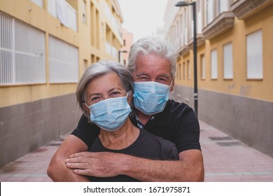 couple of two seniors wearing medical mask to prevent coronavirus (covid-19) or another type of virus - close up of faces in middle of street -  protect happy cheerful people looking at the camera fun
