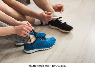 Couple tying up laces on sport shoes closeup. Unrecognizable man and woman preparing for training, wearing sneakers, copy space