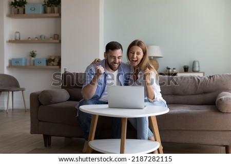 Couple use laptop read e-mail, get fantastic commercial offer discount and sell-out on-line, celebrate lottery, auction win, feel happy, look overjoyed. Moment of victory, success, achievement