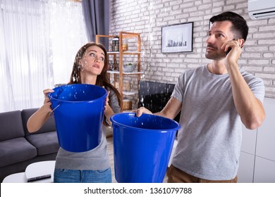 Couple Using Bucket For Collecting Water Leakage From Ceiling And Calling Plumber On Cellphone