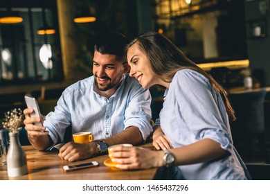 couple using cellphone while enjoying coffee in cafeteria