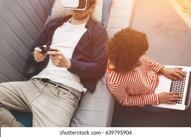 Couple Using Electronic Devices. Man Playing Breathtaking Computer Game With VR Headset. Woman Typing On Laptop. Modern Family Life