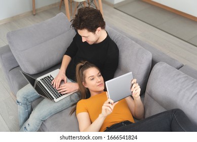 Couple Using Fast Home Internet With Laptop And Digital Tablet. Woman And Man On Sofa In Living Room